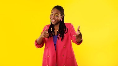Sırada sen varsın. Parlak Makyajlı Pozitif Siyahi Kadın, Stüdyoda Sarı Arkaplan Üzerine Duran Kamera Pozisyonunu Gösteriyor. Ben seni seçiyorum. Panoramik Çekim