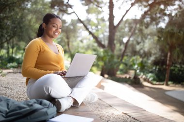 E-öğrenme. Laptop kullanan neşeli Brezilyalı bayan öğrenci, parkta ya da üniversite kampüsünde otururken uzaktan öğreniyor, kopyalama alanı. Modern online eğitim