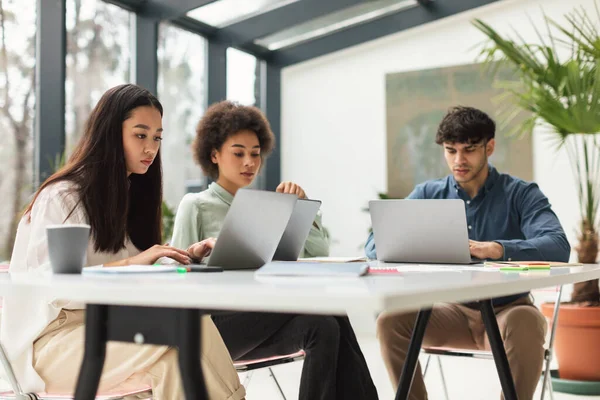商业团队 在现代办公室 三名多族裔同事使用笔记本电脑坐在桌旁工作 企业生活方式的概念 有选择地关注年轻的亚洲女商人 — 图库照片