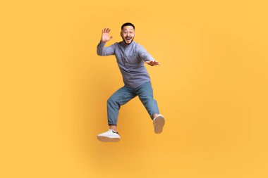 Kaygısız genç Asyalı adam sarı stüdyo arka planında havaya atlıyor, mutlu milenyum adamı olumlu duygularını ifade ediyor, kandırıyor ve eğleniyor, tam boy çekim yapıyor, boşluğu kopyalıyor.