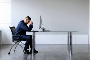 Orta yaşlı bir ofis çalışanının fazla mesai yapmaktan, bilgisayarlı masada oturmaktan, fotokopi alanından bıkmış halinin yan görüntüsü. Bitkin işadamı projeyle ilgili sorun yaşıyor