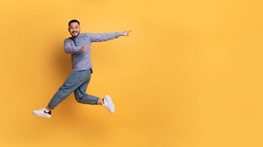 Şuna bir bak. Cherful Asyalı adam havaya zıplarken kenara çekiliyor, olumlu genç milenyum erkeği eğleniyor ve sarı stüdyo arka planında bedava fotokopi alanı gösteriyor, panorama