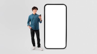Telefondaki gülümseyen adam, Beyaz Stüdyo Arkaplanı Üzerinde Uygulama Reklamı İçin Boş Ekranlı Dev Akıllı Telefonun yanında Olumlu Mesaj Mesajları okuyor. Panorama, Mockup