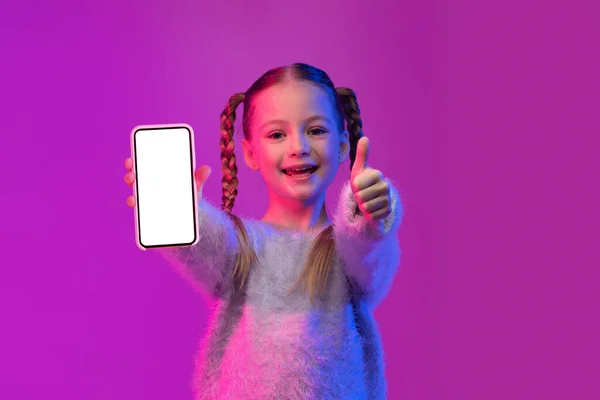 儿童移动应用程序不错 快乐可爱的少女 留着辫子 带着白色的空白屏幕模型展示手机 用大拇指在色彩艳丽的背景上 复制空间 — 图库照片