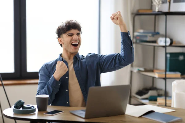 業績の喜び 現代のオフィスで大きな運座りを祝うノートパソコンの揺れ拳で中東の男 感情的な若いビジネスマンジェスチャーはい 成功した仕事を叫んで — ストック写真
