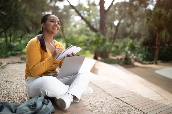 屋外のウェビナーに出席し 公園に座って ノートパソコンを使用してノートを取り スペースをコピーする陽気なブラジル人女性 E教育 トレーニング オンラインコース — ストック写真