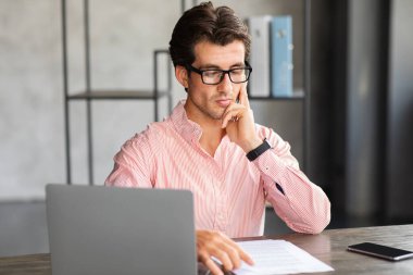 Kariyer, girişimcilik gibi. Konsantre olmuş yakışıklı milenyum adamı resmi kıyafetler giyiyor, gözlük proje yöneticisi dizüstü bilgisayarın önünde oturuyor, belgeleri okuyor, ofiste çalışıyor, boşluğu kopyalıyor.