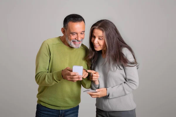 stock image Positive curious caucasian aged couple in casual reading messages on smartphone, chatting in social network, isolated on gray background, studio. Blog, communication remotely app, ad and offer