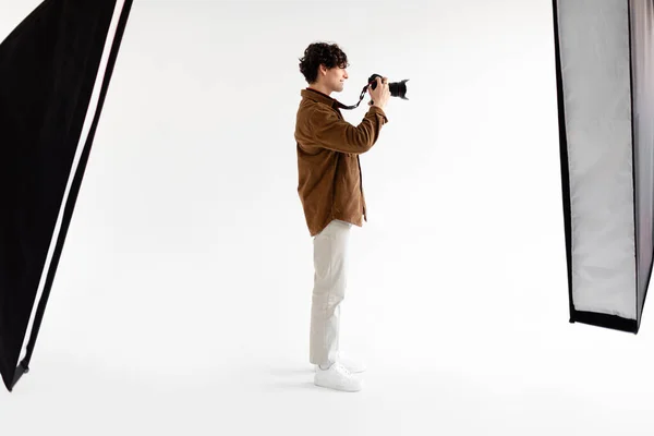全长摄影年轻摄影师手持专业摄影相机 站在白色背景上 配有现代设备 侧视图 — 图库照片