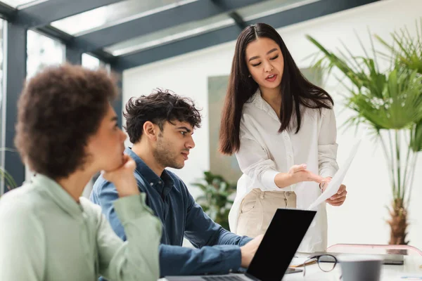 Diverse Business Team Analyzing Mistakes And Problems Working On Project, Businesswoman Showing Paper To Coworkers Discussing Work During Corporate Meeting In Modern Office. Selective Focus