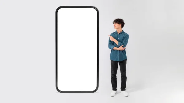 拥有一个巨大智能手机的年轻人广告空白应用空间 站在白色背景上指向手机屏幕 盖伊广告移动提供显示大的小工具 莫科普 — 图库照片