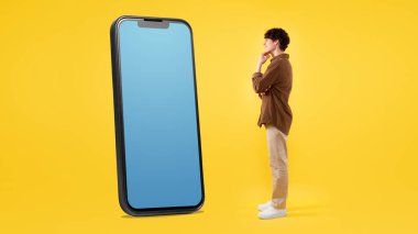 Sarı Stüdyo Arkaplanındaki Boş Uygulama Ekranını Gösteren Büyük Cep Telefonlu Heyecanlı Genç Adam Pozu. Heyecanlı bir şekilde telefon ekranına bakan adam mobil reklam teklifinde bulunuyor. Panorama