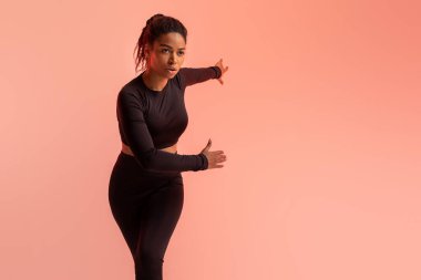 Aktif yaşam tarzı konsepti. Atletik siyahi kadın şeftali neon arka planı üzerine antrenmandan önce ısınıyor. Fit kadın esneklik egzersizleri yapıyor.