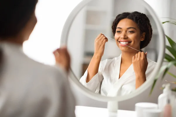 口腔ケア 自宅でミラーの近くに歯科フロスを使用して黒の女性を笑顔 美しい若いアフリカ系アメリカ人女性のクレンジング歯 毎日の衛生ルーチンを作ります 反射に選択的な焦点 — ストック写真