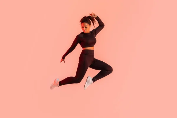 フィットネスライフスタイル 桃のネオンスタジオの背景の上に空気中でジャンプする動機黒の女性 運動選手の女性は ジャンプ演習を作ります カーディオワークアウトを楽しんで フル長さ コピースペース — ストック写真
