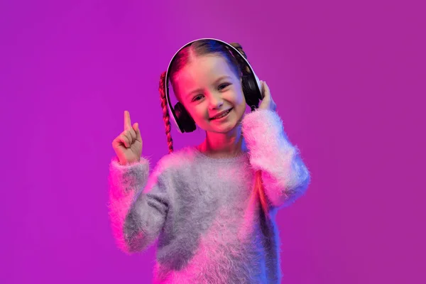 用现代立体声无线耳机在霓虹灯下的粉红工作室背景上展示手指向上的尤利卡手势 复制广告空间 音乐移动应用 — 图库照片
