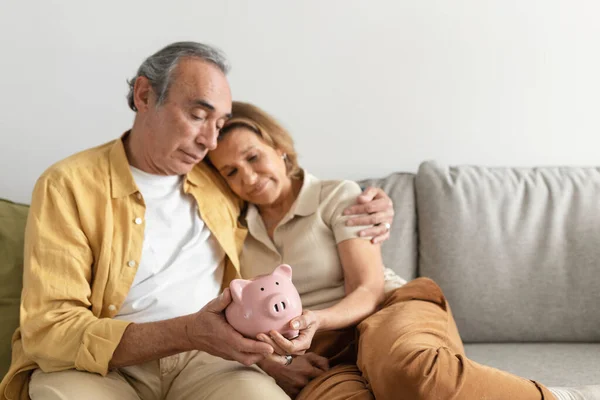 退職金だ シニア配偶者保持ピギーバンクながら一緒に座ってソファと抱擁 愛する高齢者カップル計画予算と将来のためのお金を節約 フリースペース — ストック写真
