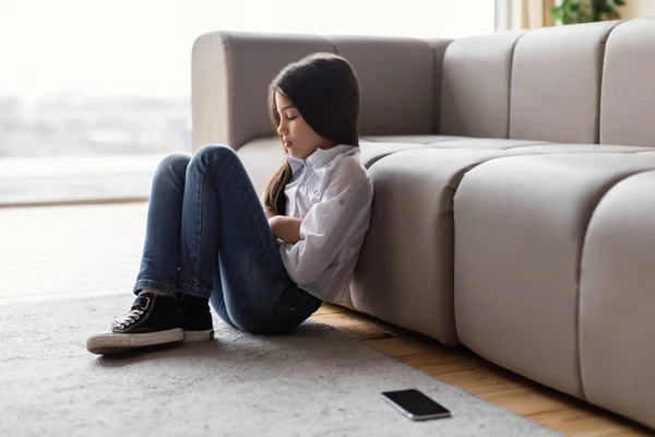 Loneliness In Digital Age. Depressed Girl Sitting Near Abandoned Phone Suffering From Lack Of Communication And Depression At Home, Hugging Herself Feeling Upset. Social Media And Kid Mental Health