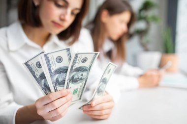 Para sayan genç bir kadın, elinde dolar banknotları, seçici odak, yakın çekim, boş alan. Vergi, durgunluk ekonomisi, enflasyon, yatırım, finans, tasarruf, maaş ve ödeme kavramları