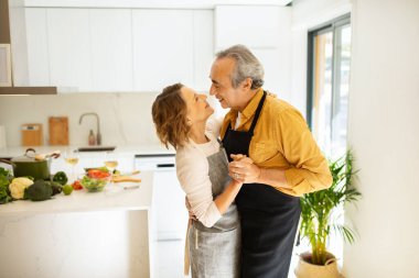 Romantik yaşlı erkek ve kadın evde birlikte dans ediyor, kıdemli eşleri seviyor mutfakta duruyor, el ele tutuşuyor, birlikte vakit geçiriyorlar.