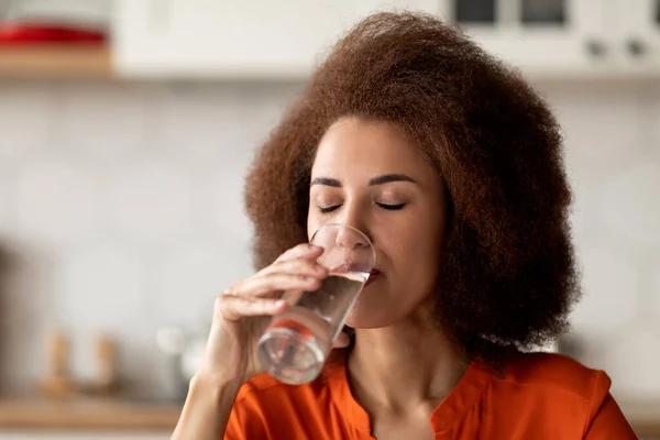 Ung Afrikansk Amerikansk Kvinde Drikker Rent Mineralvand Fra Glas Derhjemme - Stock-foto