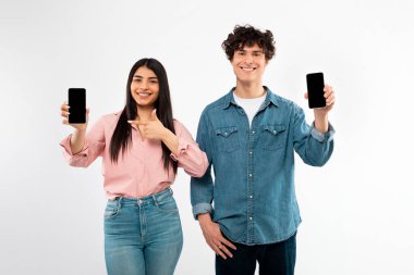 Harika bir uygulama. Neşeli genç çift cep telefonlarını boş ekranlarla gösteriyorlar, Gadget 'ları işaret ediyorlar, gençlere beyaz arka planda poz vermeleri için mobil uygulama öneriyorlar. Stüdyo Çekimi, Model