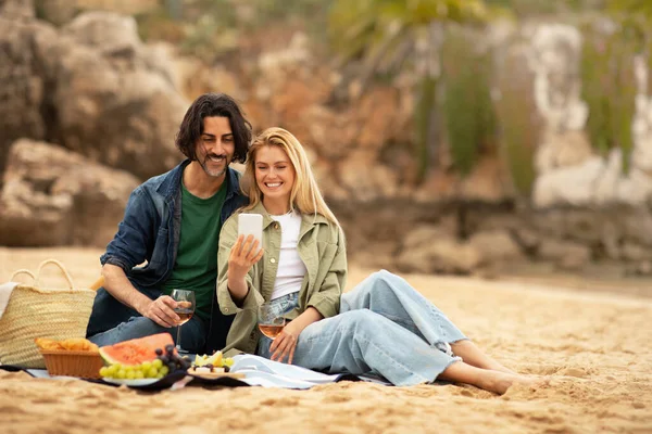 浪漫的年轻夫妇在阳光明媚的海滩野餐时自拍 快乐的欧洲男人和女人在海滨放松 摆姿势在手机前拍照 复制空间 — 图库照片