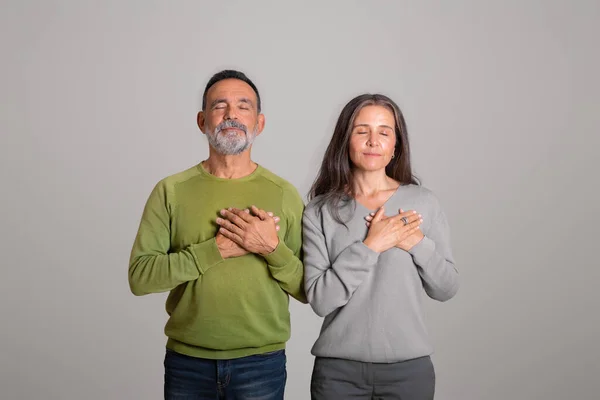 双目紧闭的积极的高加索老年夫妇做感恩的手势 把手放在胸前 隔离在灰色背景下 在工作室里 人们的情感 爱的签署 广告和提供 — 图库照片