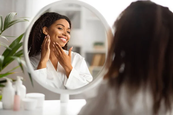 美しいアフリカ系アメリカ人女性の顔に触れ 自宅で鏡を見て 幸せな魅力的な黒人女性彼女の完璧な肌を楽しんで 笑顔の女性は スキンケアルーチンを作る 選択的フォーカス — ストック写真