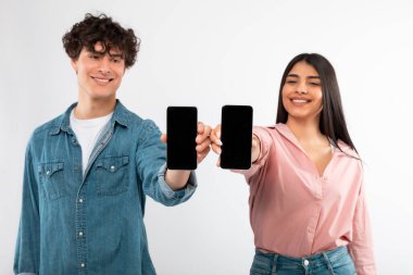 Mobil Teklif. Kameraya Akıllı Telefonlar Gösteren, Uygulama Reklamı İçin Boş Ekranlar Gösteren Beyaz Stüdyo Arkaplanının Üzerinde Duran Mutlu Genç Çift. Seçici Odaklanma, Model