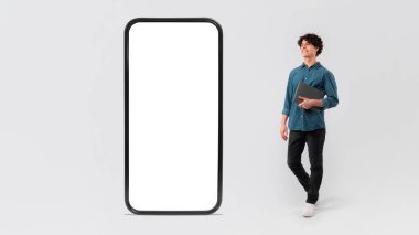 Laptop Poz Veren Genç Adam Beyaz Stüdyo Arkaplanında Boş Ekran ile Cep Telefonu Reklam Uygulaması Mobil Teklifi. Gadget ve Teknoloji Konsepti. Model