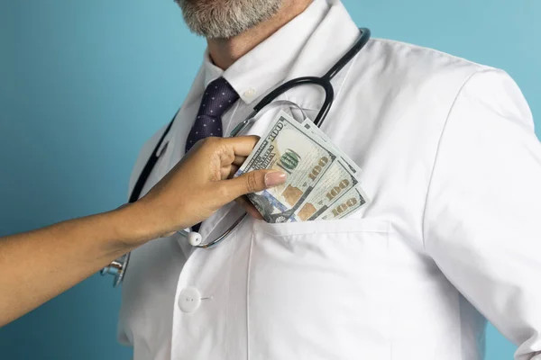 医院腐败 医疗保健 医学概念 病人手把钱钞票放进医生外套口袋 蓝色工作室背景 复制空间 — 图库照片