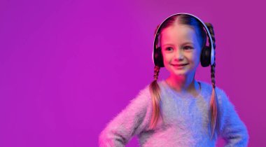 Çocuk konsepti için müzikal mobil uygulama. Sevimli, sevimli, güzel, sarışın, sıradan, kablosuz kulaklık takan, fotokopi alanına bakan, gülümseyen küçük kız.