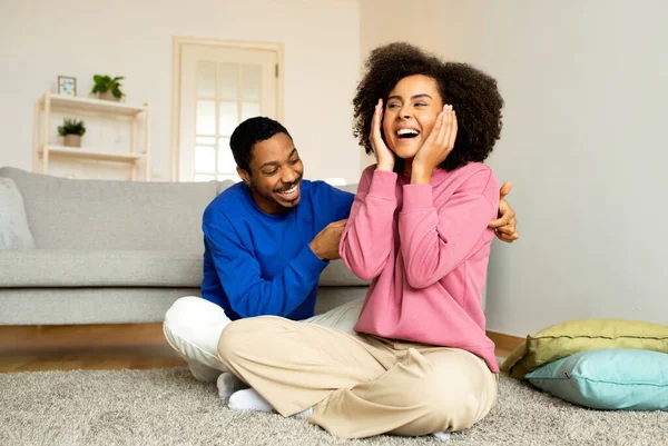 愛と笑い アフリカ系アメリカ人の若いカッドリング 夫は楽しそうに妻をくすぐる 一緒に自宅で座って楽しんでいます 週末に絆を結ぶ配偶者 喜びを共有する瞬間を楽しむ — ストック写真