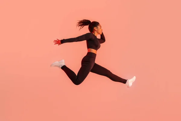 stock image Athlete black woman in sportswear jumping and having workout on red neon studio background, side view, copy space, full length. Sport and fitness concept