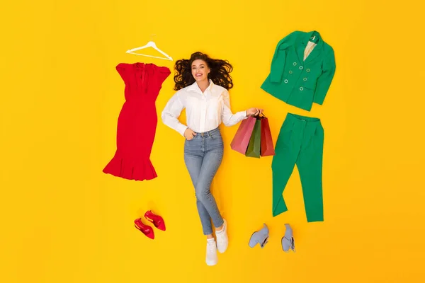 Neşeli Moda Kadını Alışveriş Torbaları Tutuyor Farklı Giysilerin Arasında Yatıyor — Stok fotoğraf