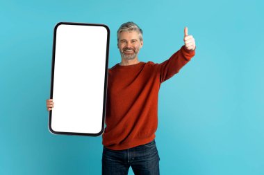Harika bir teklif, güzel mobil uygulama. Neşeli, yakışıklı, gri saçlı, sakallı, olgun bir adam. Sıradan, büyük bir telefonla beyaz ekran, model, baş parmağını gösteren, mavi stüdyo geçmişi olan.