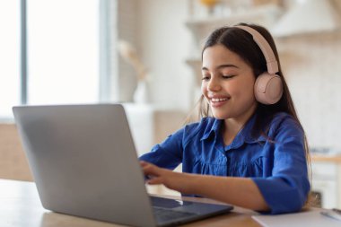 E-öğrenme sınıfı. Evde oturan kulaklıkları takmış, bilgisayarında daktilo yazan neşeli Arapça öğrencisi kız. Liseli Kız İnternet Sörfü Mesafe Dersinin Tadını Çıkartıyor