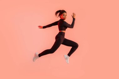 Genç, sportif siyah kadın, kırmızı neon stüdyo arka planında eğitim görüyor, koşuyor ve kameraya bakıyor, tam boy. Modern spor, aksiyon, hareket konsepti