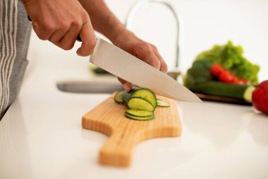 Mutfak Malı, Yemek Pişirme. Modern mutfağın tahta kesme tahtasındaki salatalıkla taze salatalık kesen Kara Erkek Elleri 'nin yakın çekimi. Kesilmiş Vuruş. Sağlıklı Gıda Hazırlama ve Tarifleri