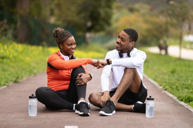 Neşeli genç siyah çift yolda oturuyor, su şişeleriyle rahatlıyor, yumruk tokuşturuyor, yazın iyi bir sonuç elde ediyorlar. Spor, başarılı dış spor, egzersiz, vücut bakımı ve ilişki