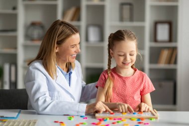 Disleksi tedavisi görüyor. Pediatrik Nörolog Hanım, tatlı küçük kızla terapi seansı yapıyor, Masaya renkli harflerle konuşan, okuma becerilerini geliştiren, yakın çekim yapan,