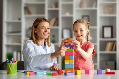 Oynayarak Öğrenmek. Ofiste terapi sırasında tahta tuğla oyunu oynayan sevimli küçük kız ve çocuk gelişimi uzmanı. Yeteneklerini geliştiren ve oyun oynamaktan zevk alan mutlu bayan çocuk.