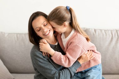 Neşeli beyaz orta yaşlı anne küçük kızına sarılıyor, hafta sonları oturma odasının içinde güzel anlar yaşıyor. Olumlu yaşam tarzı, aşk, ilişki ailesi ve evdeki iletişim