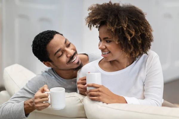 明るい幸せな若い黒のカップル自宅でコーヒーを飲むの閉鎖 喜びの千年アフリカ系アメリカ人男性と女性パジャマを着てリビングでソファに座ってお茶を楽しみチャット — ストック写真