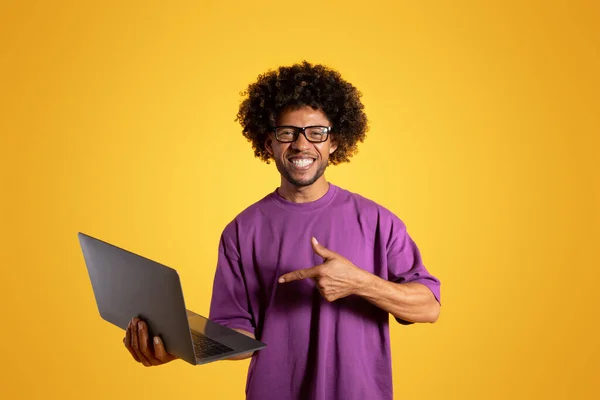 티셔츠와 안경을 곱슬머리의 남자가 노란색 스튜디오에 고립된 노트북에서 손가락을 내밀고 — 스톡 사진