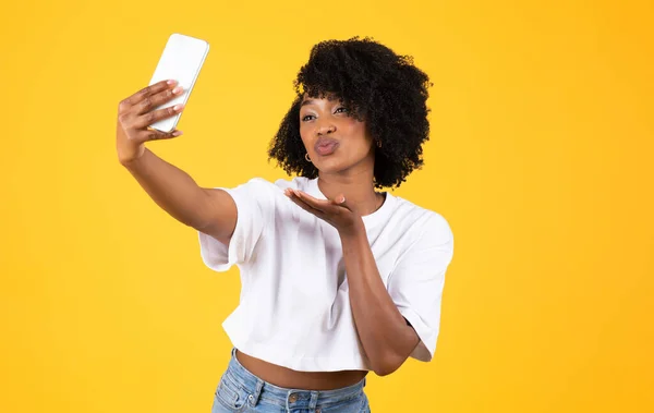 아프리카 미국인 곱슬곱슬 아가씨가 스마트폰으로 불타는 키스와 셀카를 만들고 노란색 — 스톡 사진
