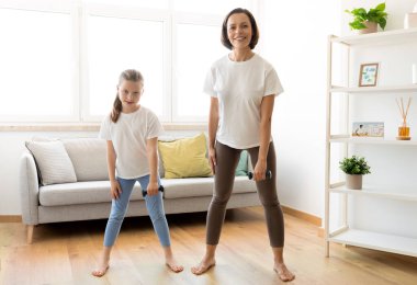 Kafkasyalı yetişkin anne ve kızı spor kıyafetleriyle el egzersizi yapıyor. Oturma odasının iç kısımlarında birlikte antrenman yapıyorlar. İlişkiler, vücut bakımı, kilo kaybı ve evde spor