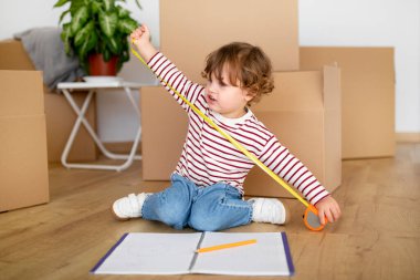 Geleceğin iç mimarı. Evde bant yöneticisiyle oynayan sevimli bir çocuk, yerde karton kutuların arasında oturan sevimli bir erkek çocuk, taşınma günü eğleniyor, boş alan arıyor.