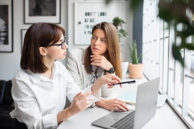 Dizüstü bilgisayarlı genç iş kadınları ofis içi işlerle ve boş alanlarla ilgili konuşuyorlar. İş beyin fırtınası, takım çalışması, profesyoneller ve fikir